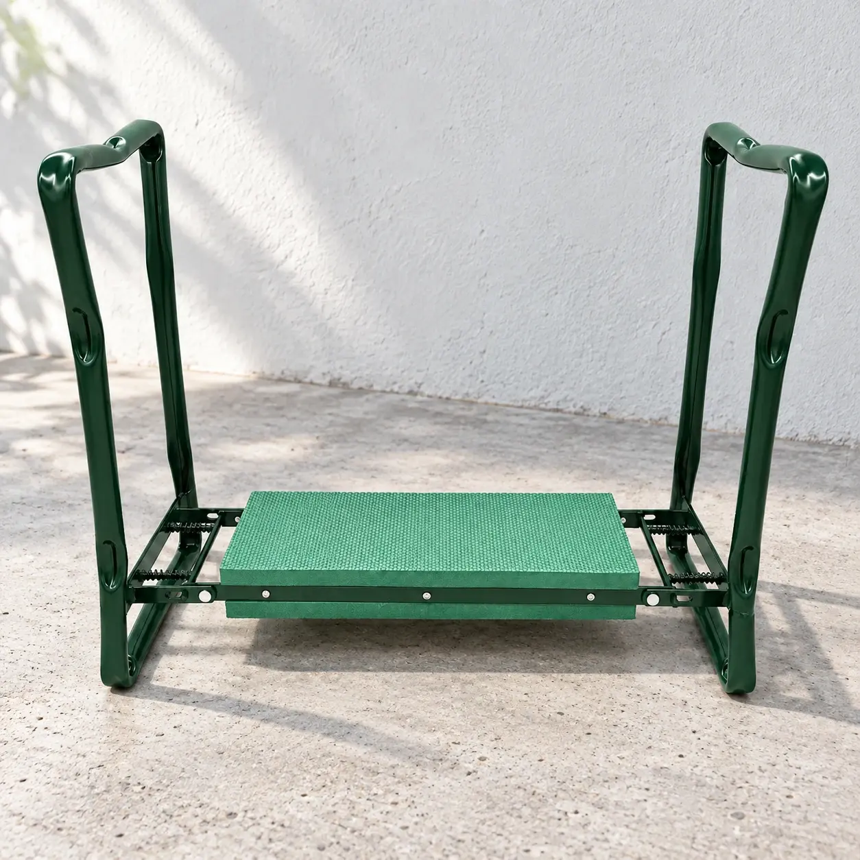 Green folding garden kneeler on a pale gray terrace